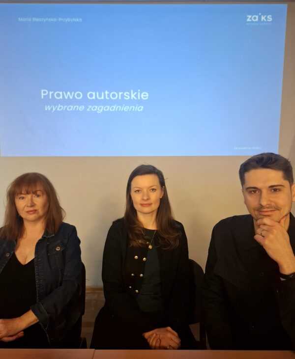 Trzy osoby siedzą za stołem na tle ekranu projekcyjnego. W centrum kobieta w ciemnym żakiecie ze złotymi guzikami, po lewej kobieta w dżinsowej kurtce, a po prawej mężczyzna w czarnej koszuli z dłonią przy brodzie. Na błękitnym ekranie widać napis "Prawo autorskie wybrane zagadnienia" oraz logo "zaiks".